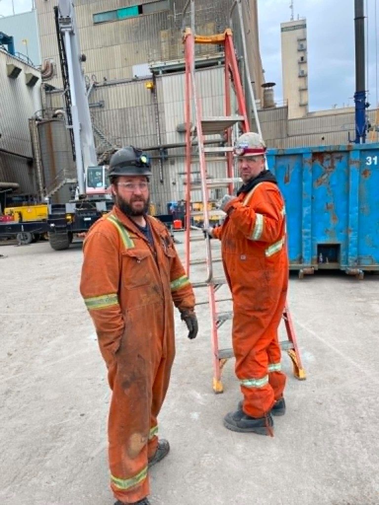 Deux mécaniciens JPSA en combinaison de sécurité orange et casques, sur un chantier industriel